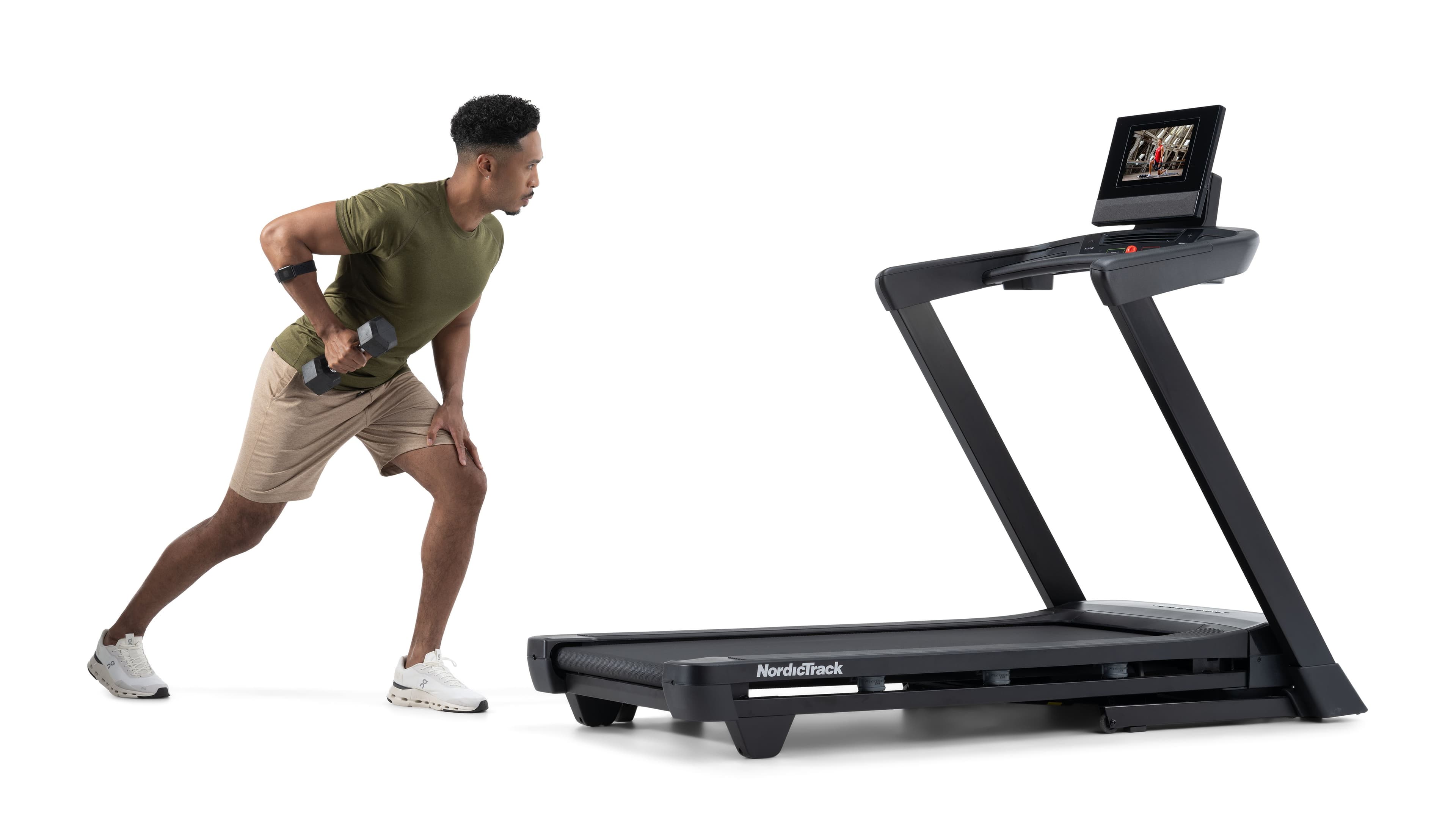 Man in athletic wear performing a dumbbell row next to a NordicTrack treadmill with an iFIT workout displayed on the touchscreen, white studio background